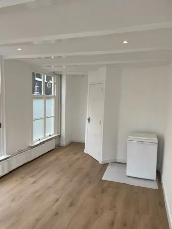 Lichte, lege kamer aan de Korte Kolksteeg met houten vloer, wit plafond met spotjes en een kleine koelkast in de hoek.